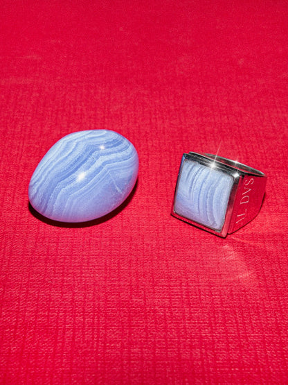 Blue lace agate stone next to a silver stone personal engraved ring on a red background